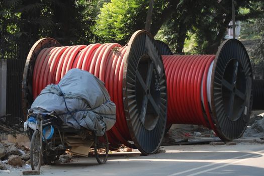 Image of large red industrial cable reels next to a covered tricycle on a sunny day.