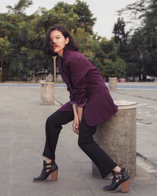 Free Woman in Maroon Long Sleeve Blazer and Black Pants Sitting on Gray Concrete  Stock Photo