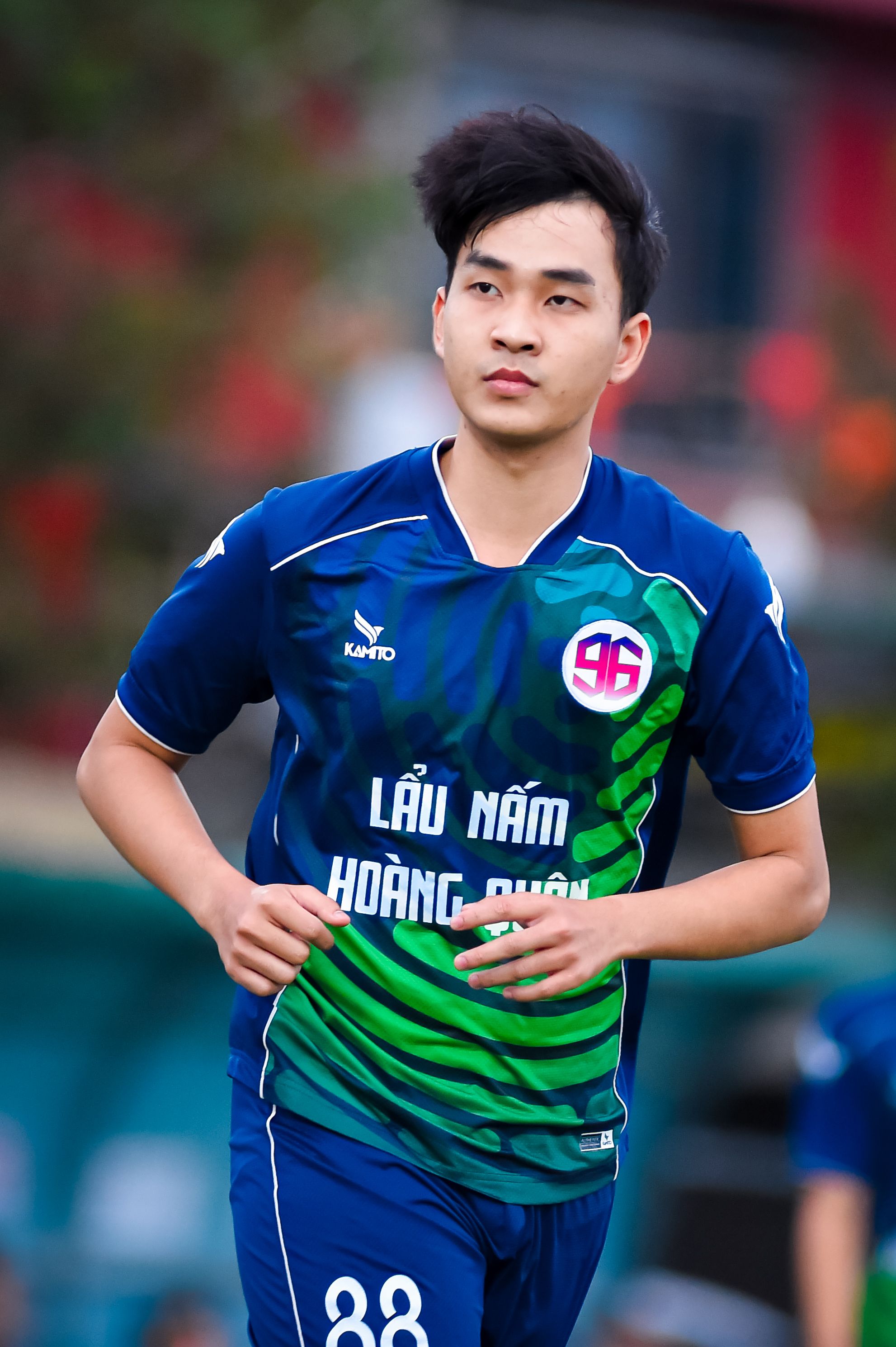 Young male football player in blue uniform running outdoors during a match in Hanoi.