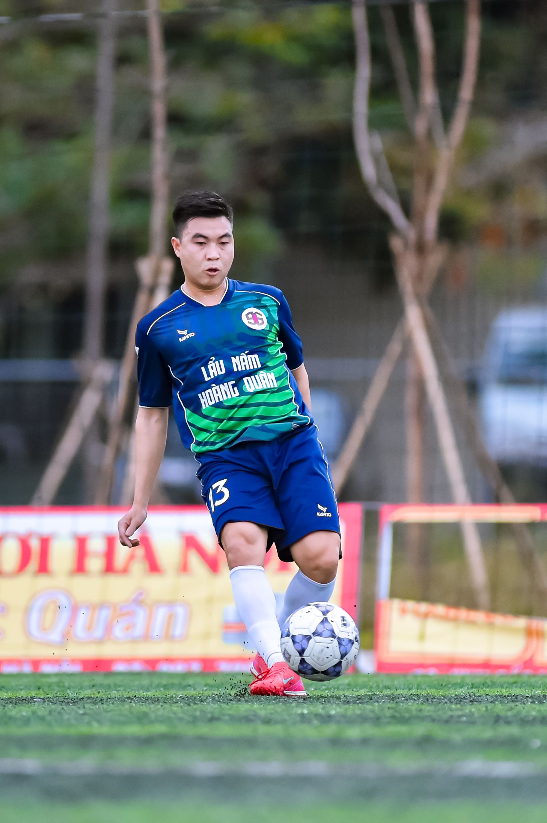 A young male footballer playing on an outdoor field in Hà Nội, Việt Nam.