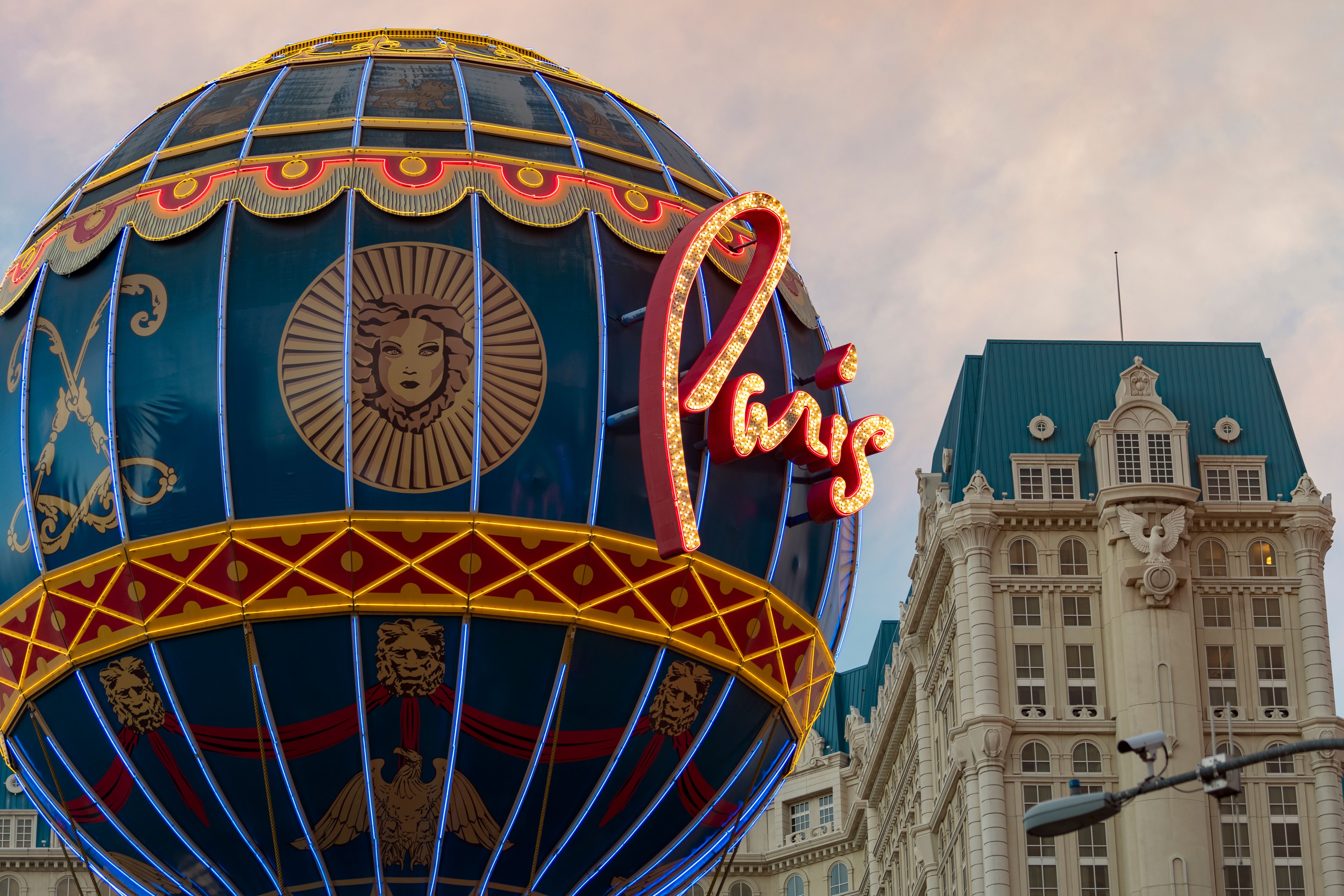 Unbeatable Grand Canyon West Bus Tour with Hoover Dam and Optional Skywalk Review Review 2026 - Illuminated Paris Hotel sign with ornate globe on cloudy evening in Las Vegas.