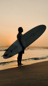 A lone surfer holds his board at sunset on a serene beach in Sri Lanka.