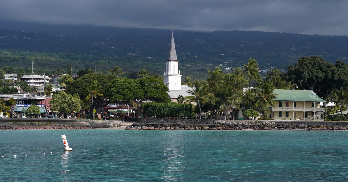 Photo by Ham Chitnupong Scenic view of Kailua-Kona waterfront featuring a historic church under cloudy skies.
