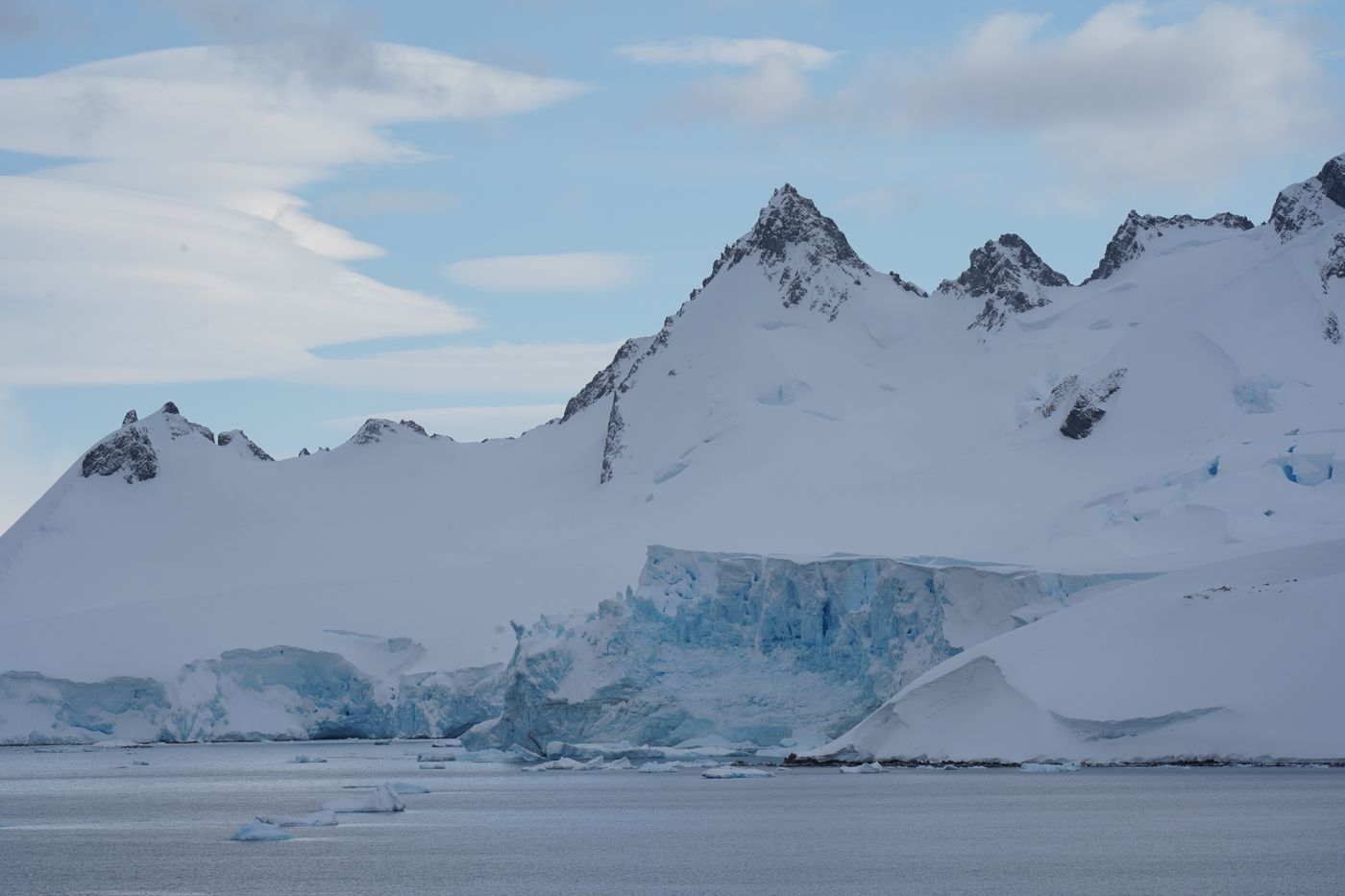 An Antarctic glacier below rugged mountain peaks under a clear blue sky
