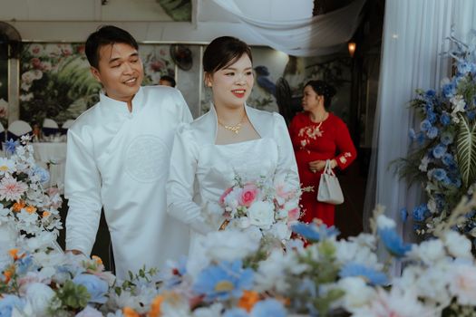 Bride and groom in elegant attire surrounded by colorful flowers at their wedding ceremony.