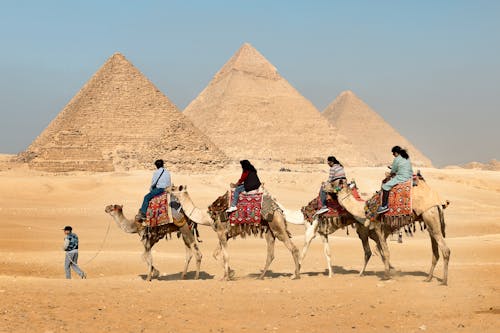 Four People Riding on Camels Across the Pyramids