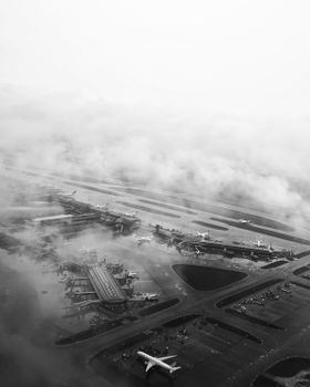 Black and white aerial shot of an airport shrouded in fog with planes on tarmac.