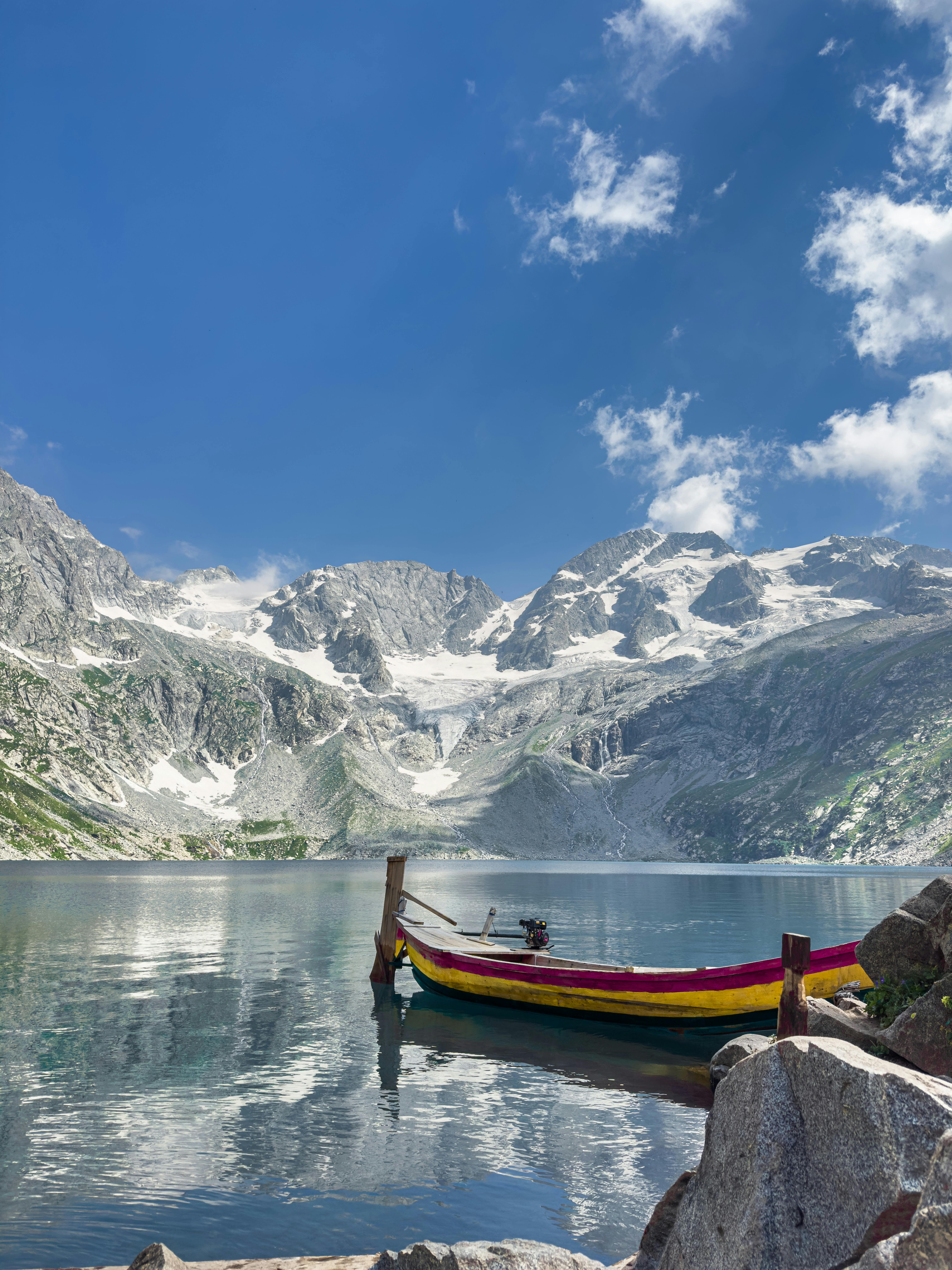 A vibrant boat floats on a serene mountain lake with snowy peaks in the background.