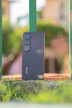 Modern smartphone rests on stone against green bars with blurred background.
