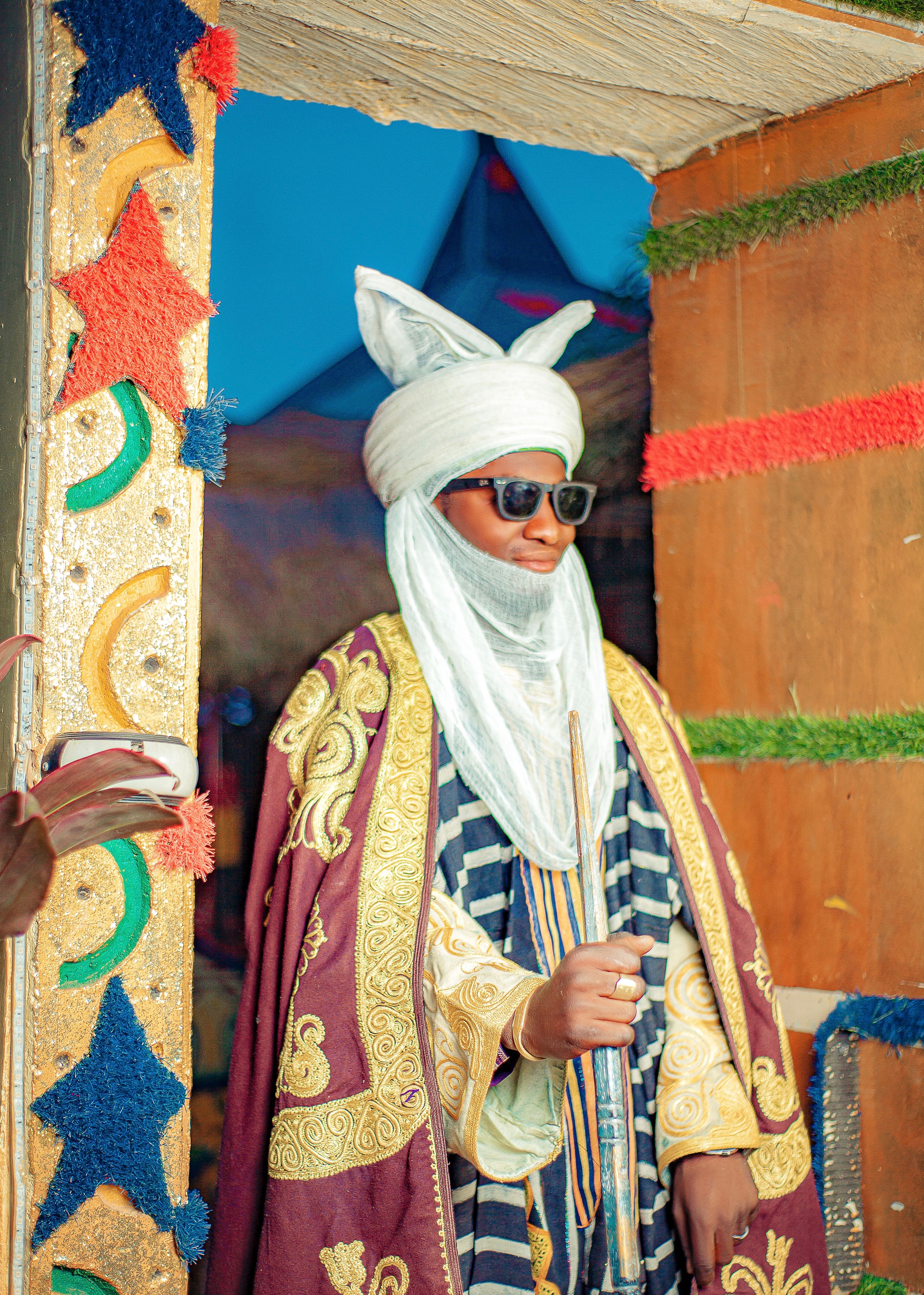 A person in traditional African attire stands in a vibrantly decorated space, showcasing rich cultural heritage.