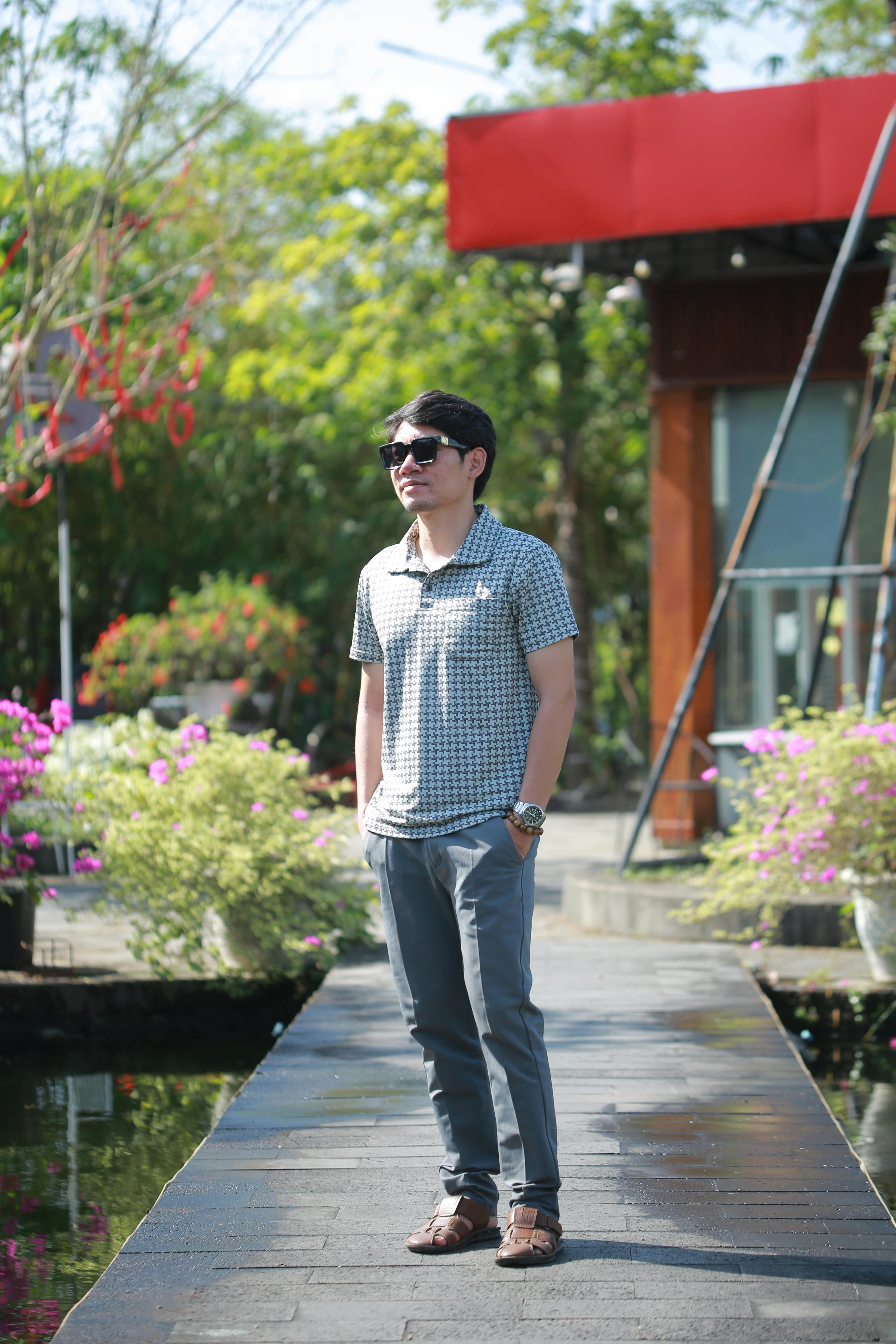 A young man in sunglasses stands confidently outdoors on a sunny day.