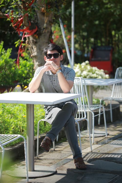 Free Casual young man enjoying sunshine at a garden cafe. Modern outdoor seating. Stock Photo