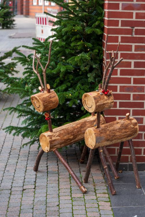 Free Festive wooden reindeer decorations outside a brick building with a Christmas tree, perfect for holiday ambiance. Stock Photo