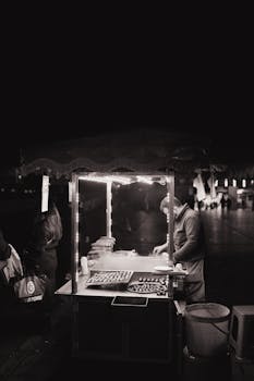 Atmospheric black and white photo of a street vendor at night under soft lights.