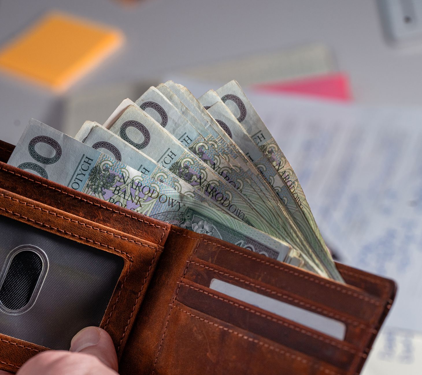 Brown leather wallet containing Polish zloty banknotes on cluttered desk