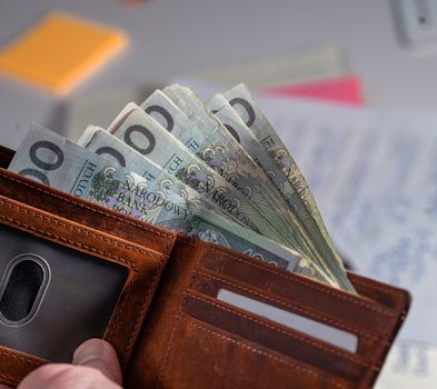 Brown leather wallet containing Polish zloty banknotes on cluttered desk
