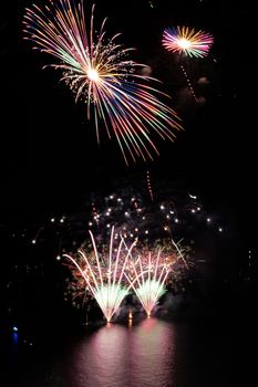 Colorful fireworks illuminate the night sky over calm water, creating a festive atmosphere.