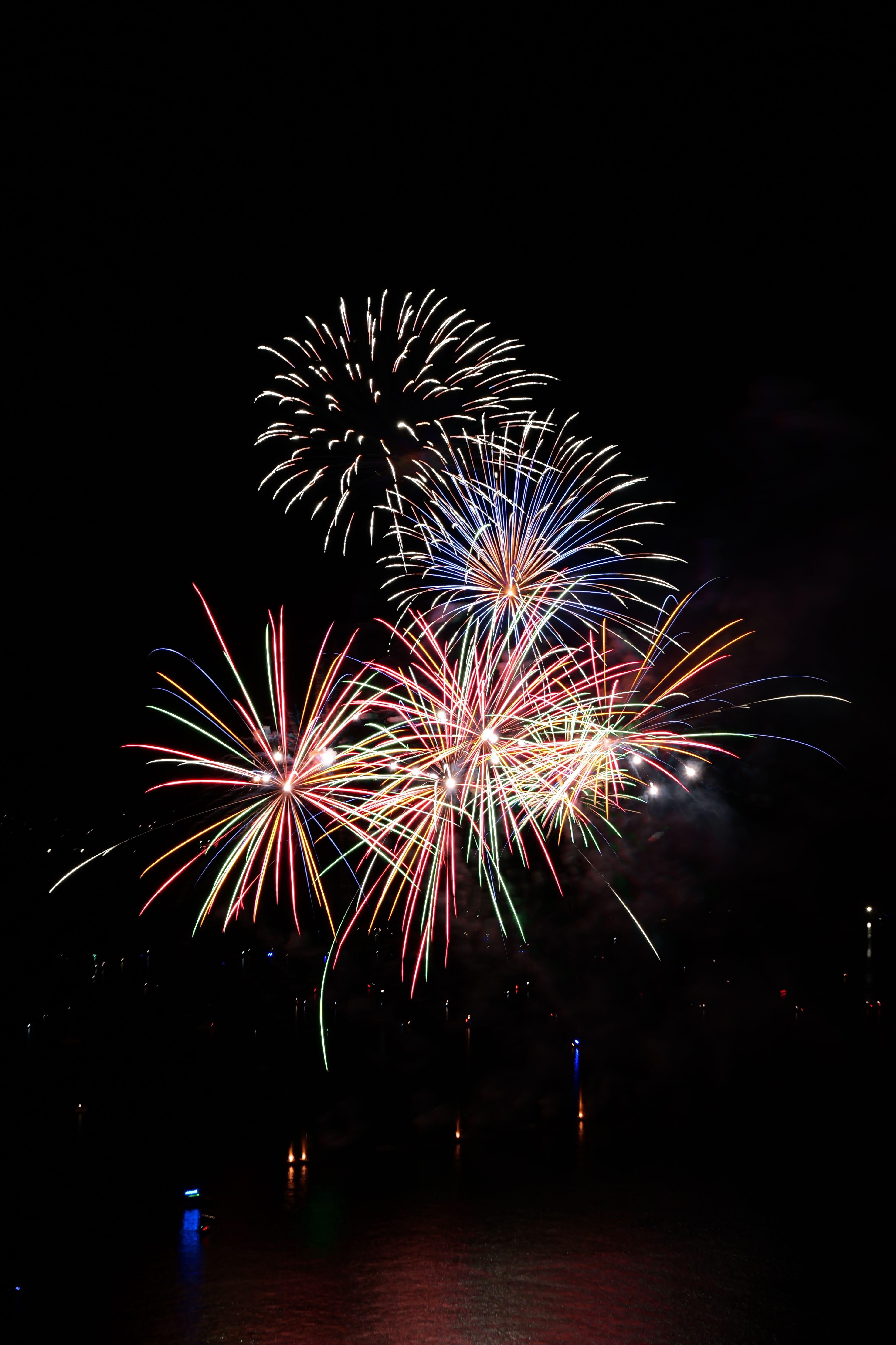 De franc Focs artificials de colors il·luminen el cel nocturn sobre una superfície d'aigua tranquil·la, creant un espectacle visual impressionant. Foto d'estoc