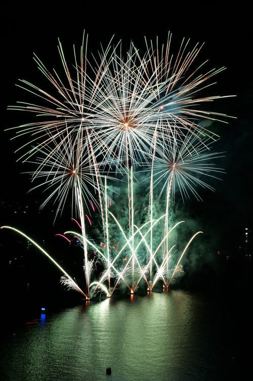 Free A vibrant fireworks display lights up the night sky, reflecting beautifully on a calm body of water. Stock Photo