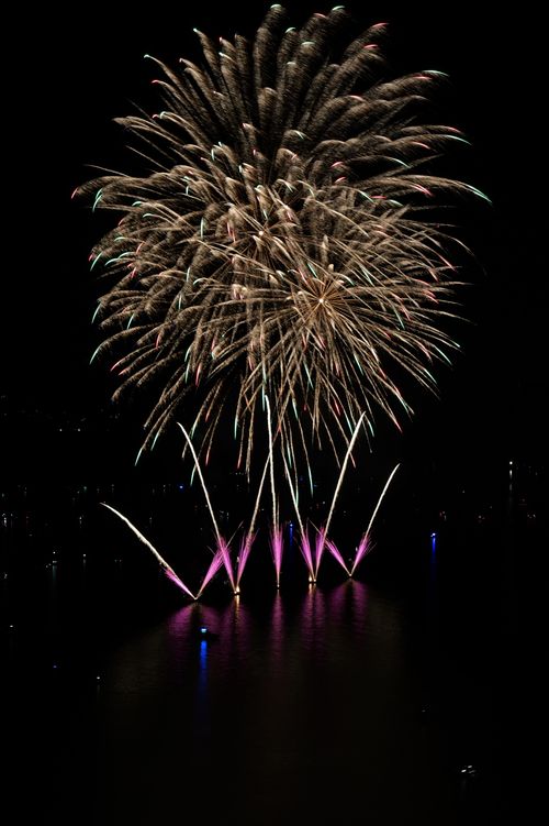 Free Vibrant fireworks illuminate the night sky over a serene water body, reflecting colorful bursts. Stock Photo