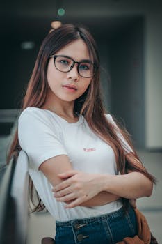 一位长发戴眼镜的年轻女子，自信地靠在室内，双臂交叉