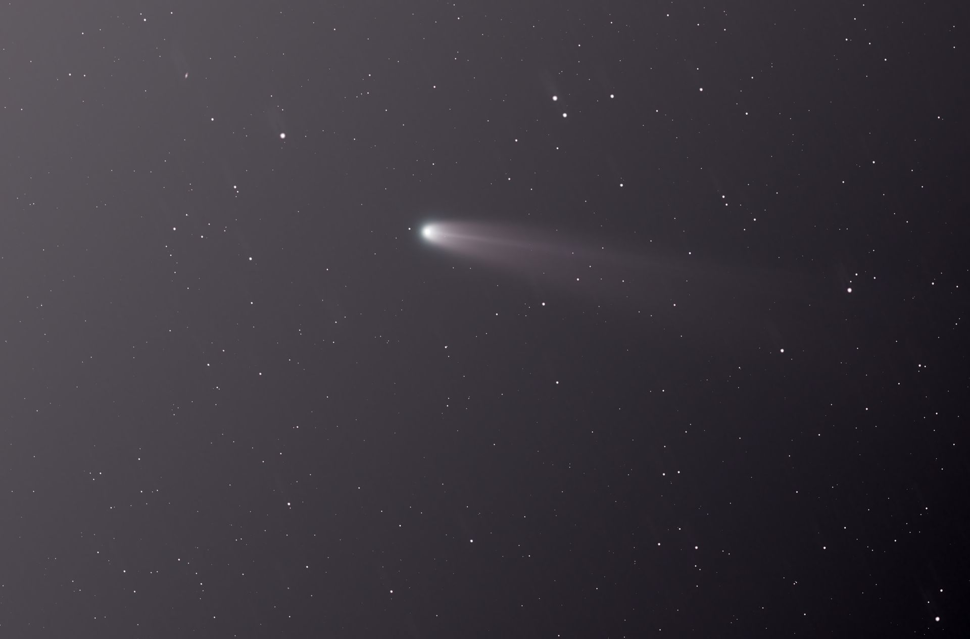 A faint comet trail across a night sky over countryside