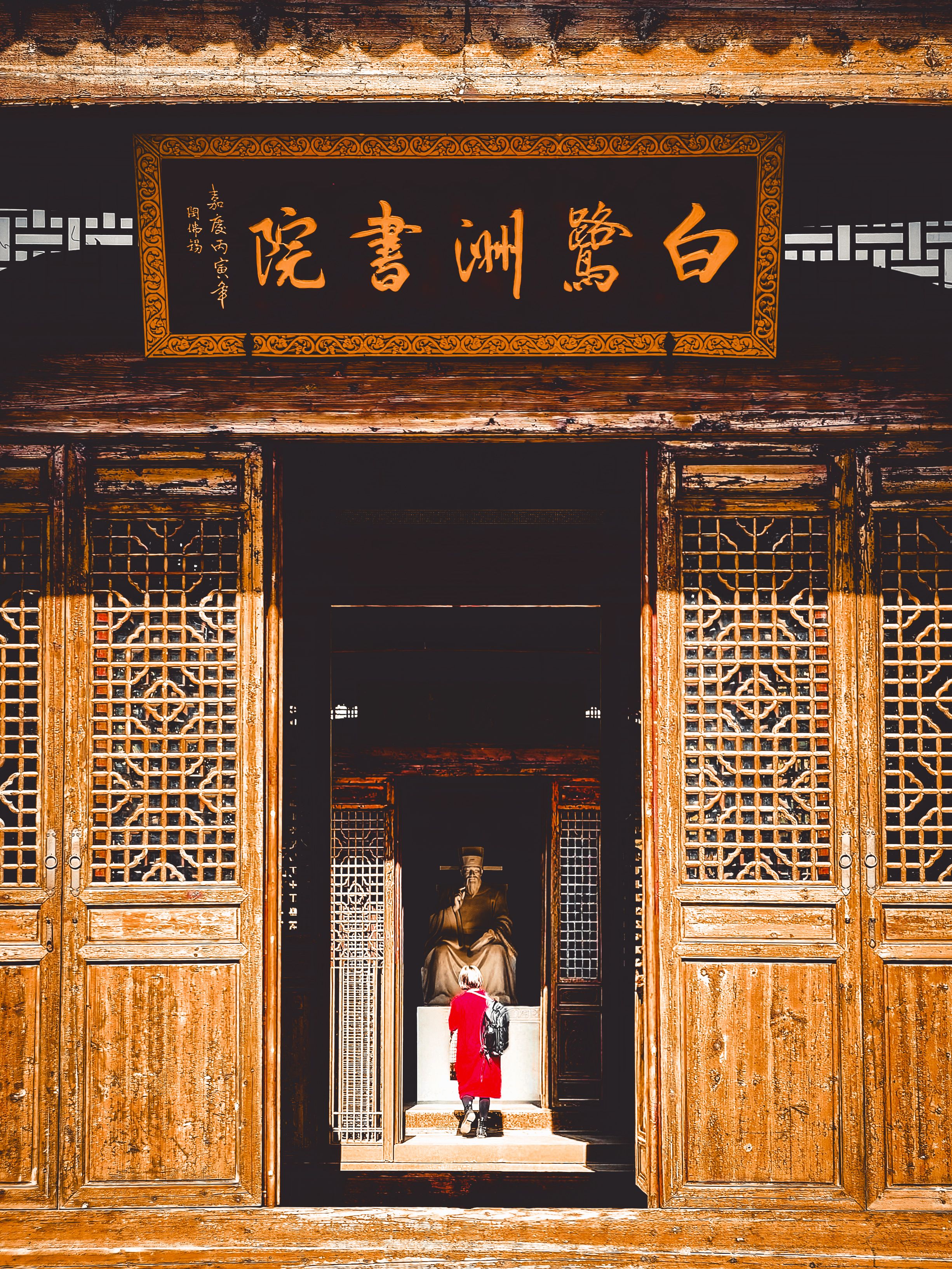 A child in red explores a wooden Chinese temple with intricate carvings.