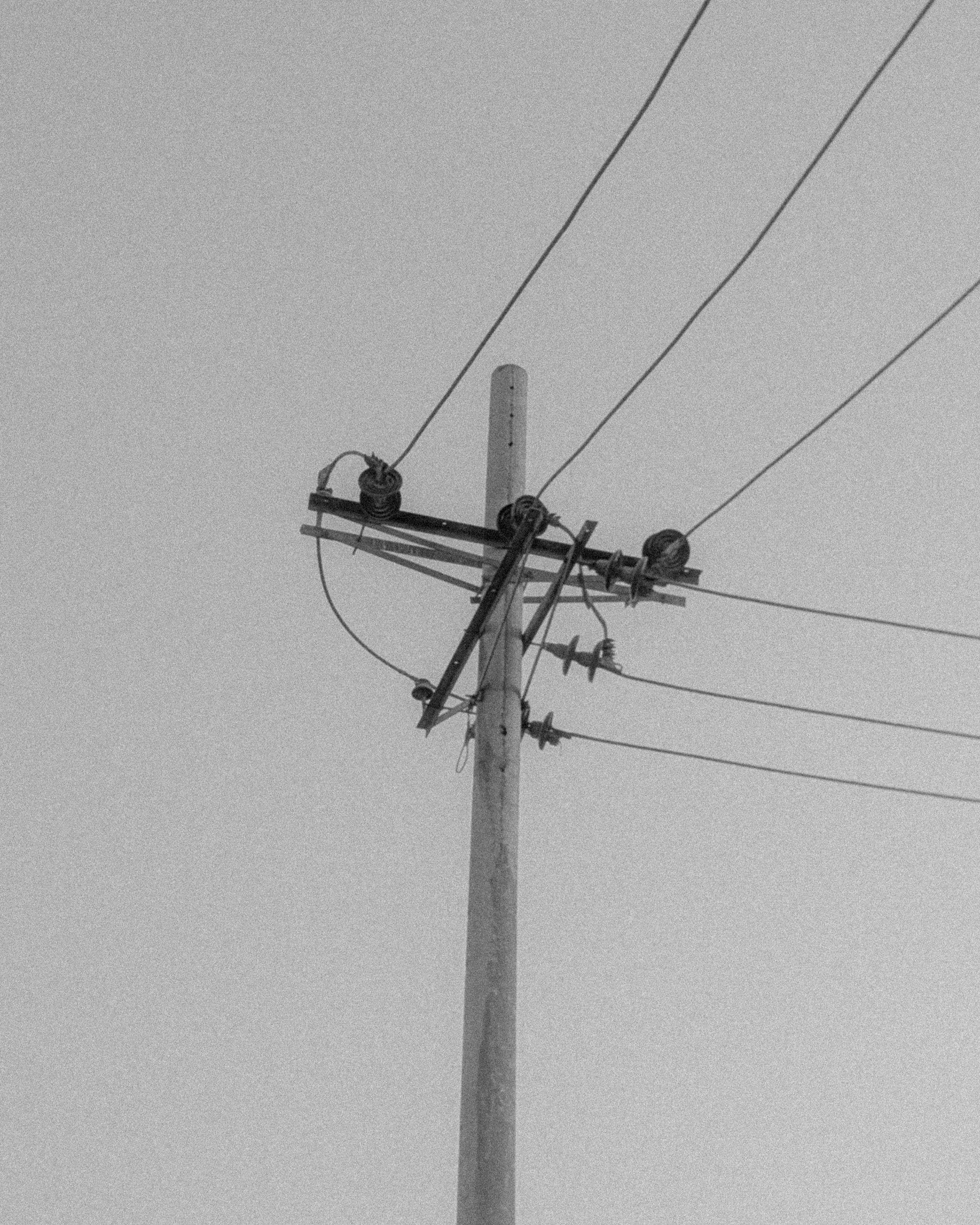 Free Minimalist black and white photo of a utility pole with intersecting wires against a clear sky. Stock Photo