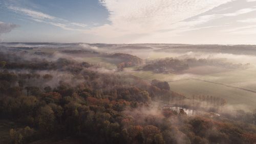 Free A serene aerial view of a foggy countryside landscape with trees and fields under a cloudy sky. Stock Photo