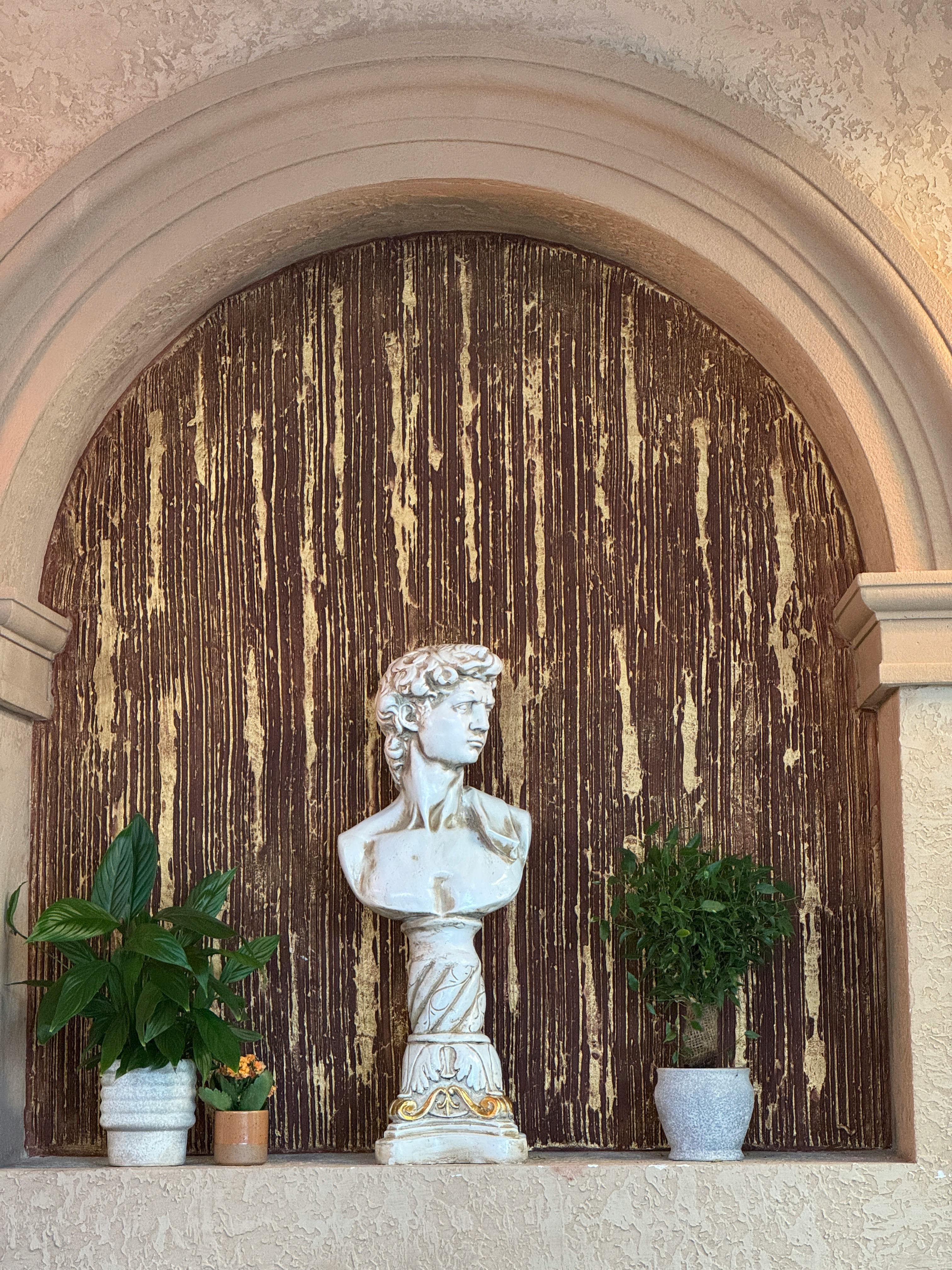 Elegant archway with classical bust surrounded by potted plants. Perfect for interior design inspiration.