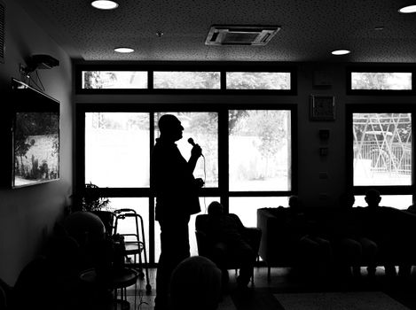 Silhouette of a person speaking indoors, with an attentive audience in the shadows.
