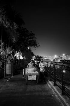 Black and white photo of two adults walking at night on a city street with lights in the background.