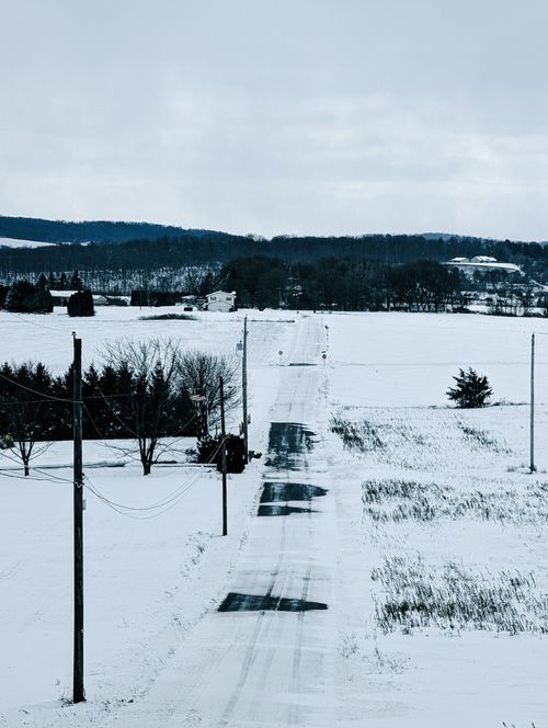 Free A tranquil winter landscape with a snow-covered road stretching into the distance amidst fields. Stock Photo
