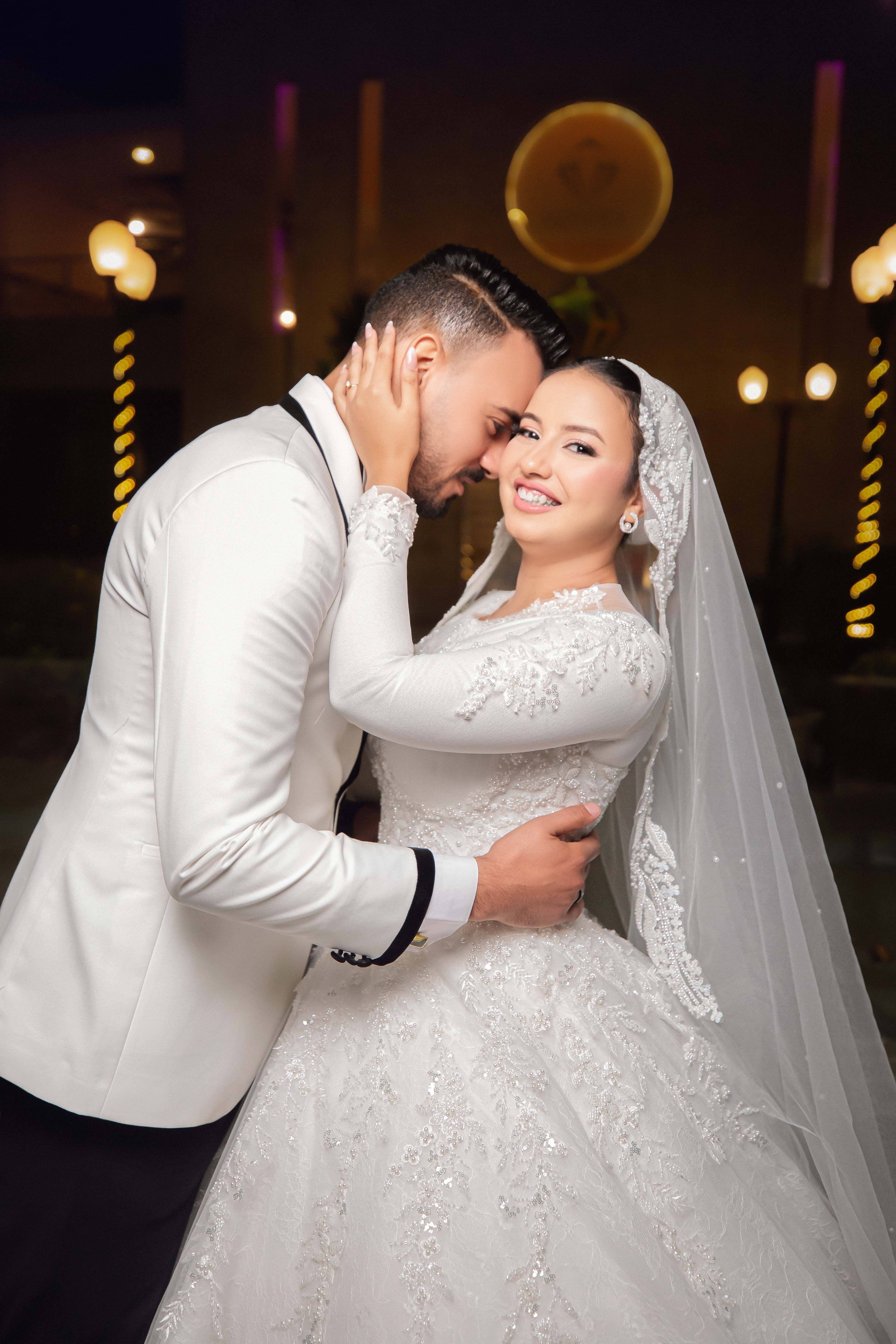 Bride and groom sharing a tender moment in elegant attire under night lights.