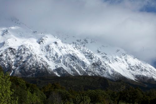 Free Stunning snow-covered mountain peaks rise above lush green forests under overcast skies. Stock Photo