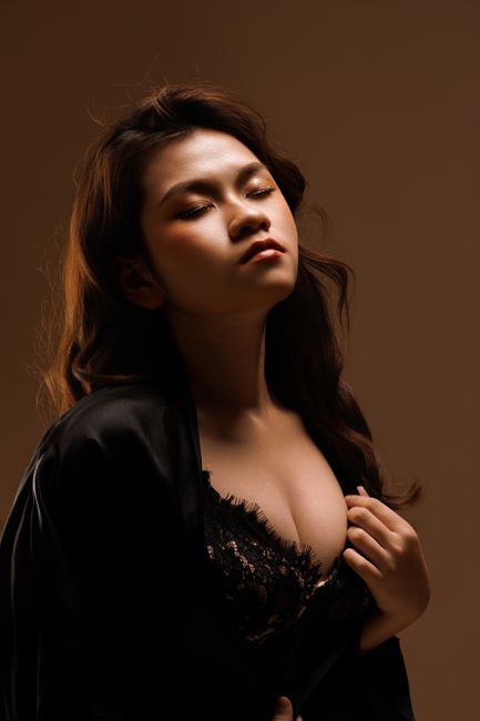 Artistic portrait of an adult Asian woman in elegant attire with soft lighting.