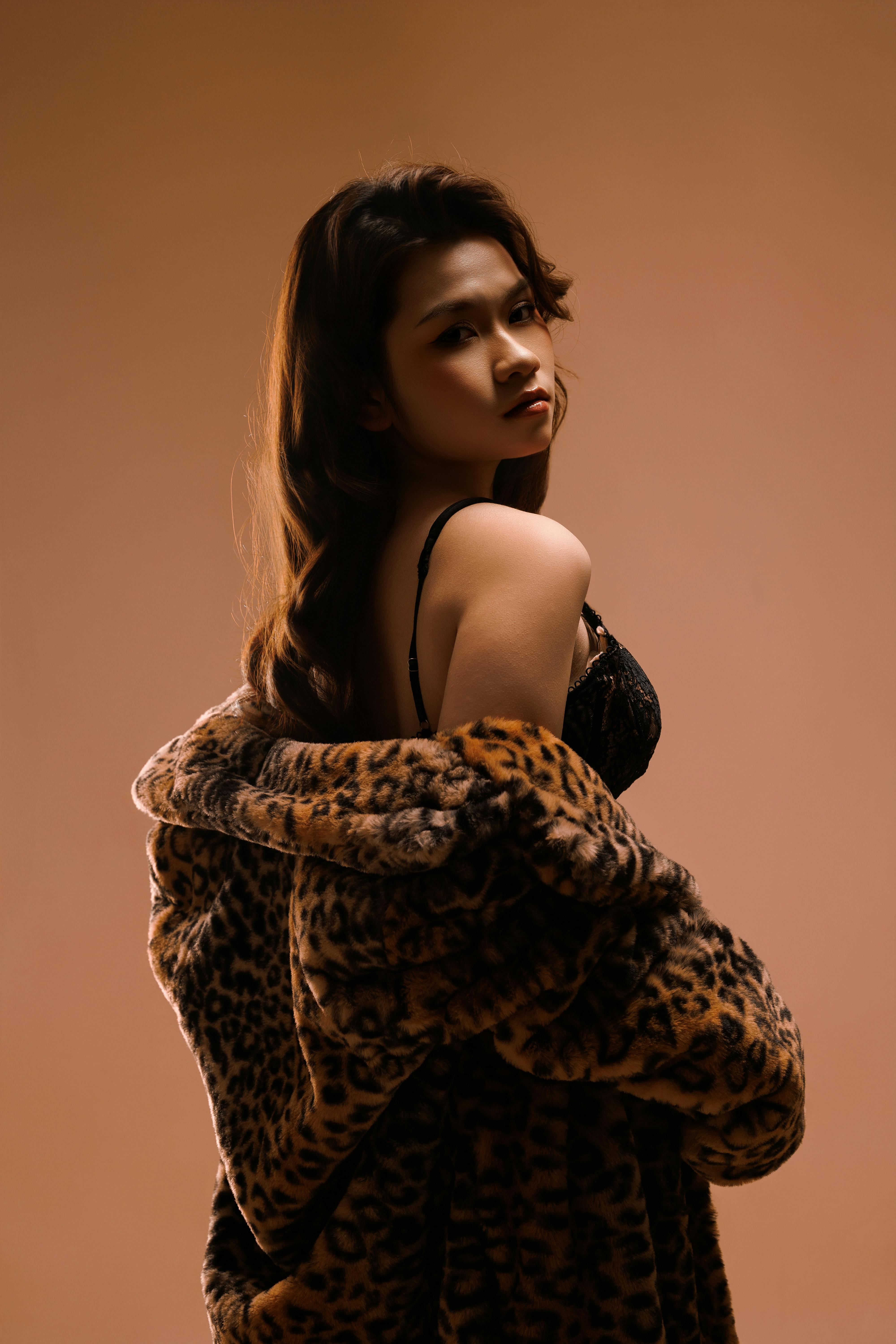Elegant woman wearing a leopard print coat and black bra posing confidently. Dramatic lighting.
