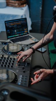 DJ manipulating audio mixer and laptop for live performance at indoor event.