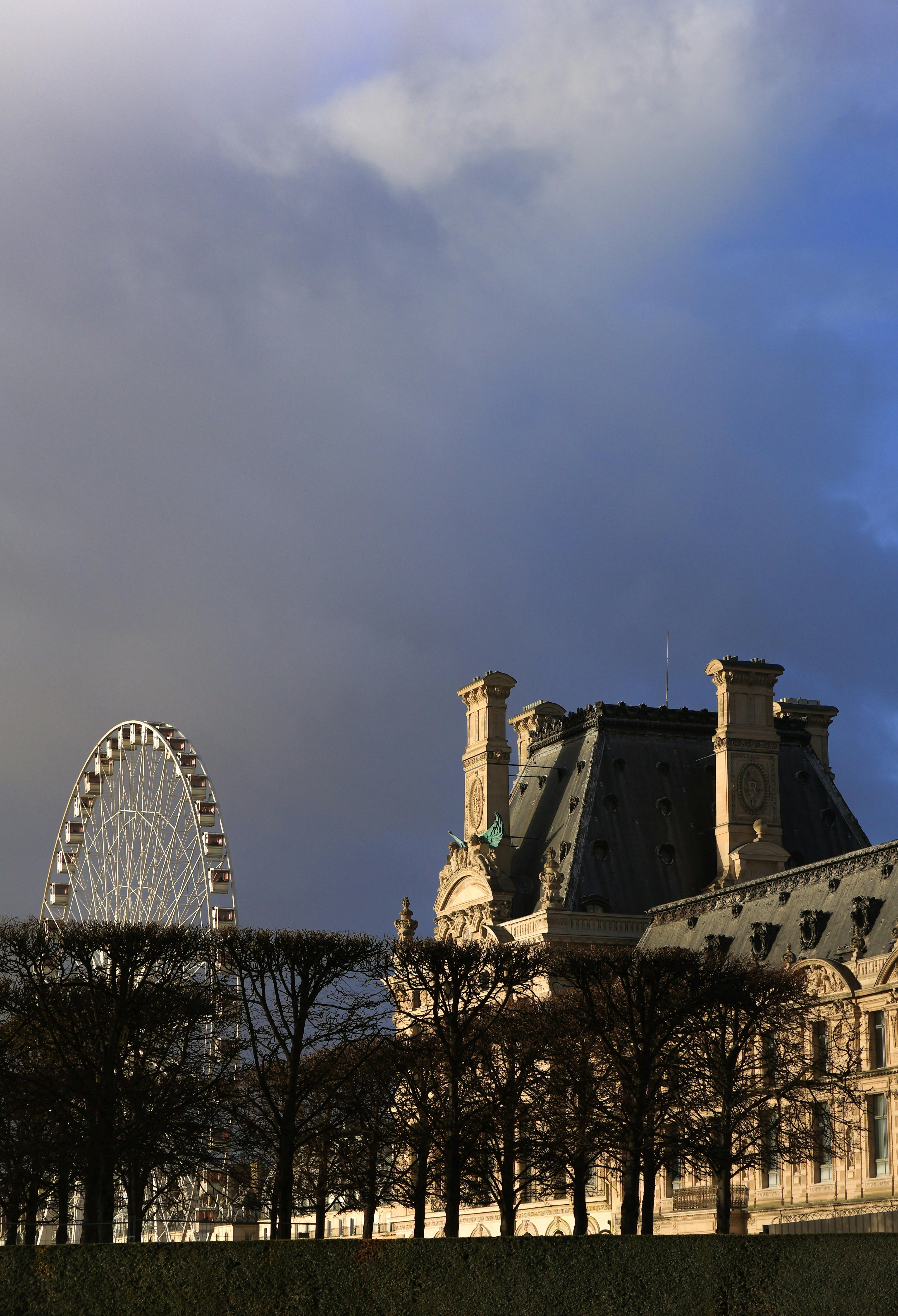 A stunning view of the Louvre Museum next to a Ferris wheel against a dramatic sky.