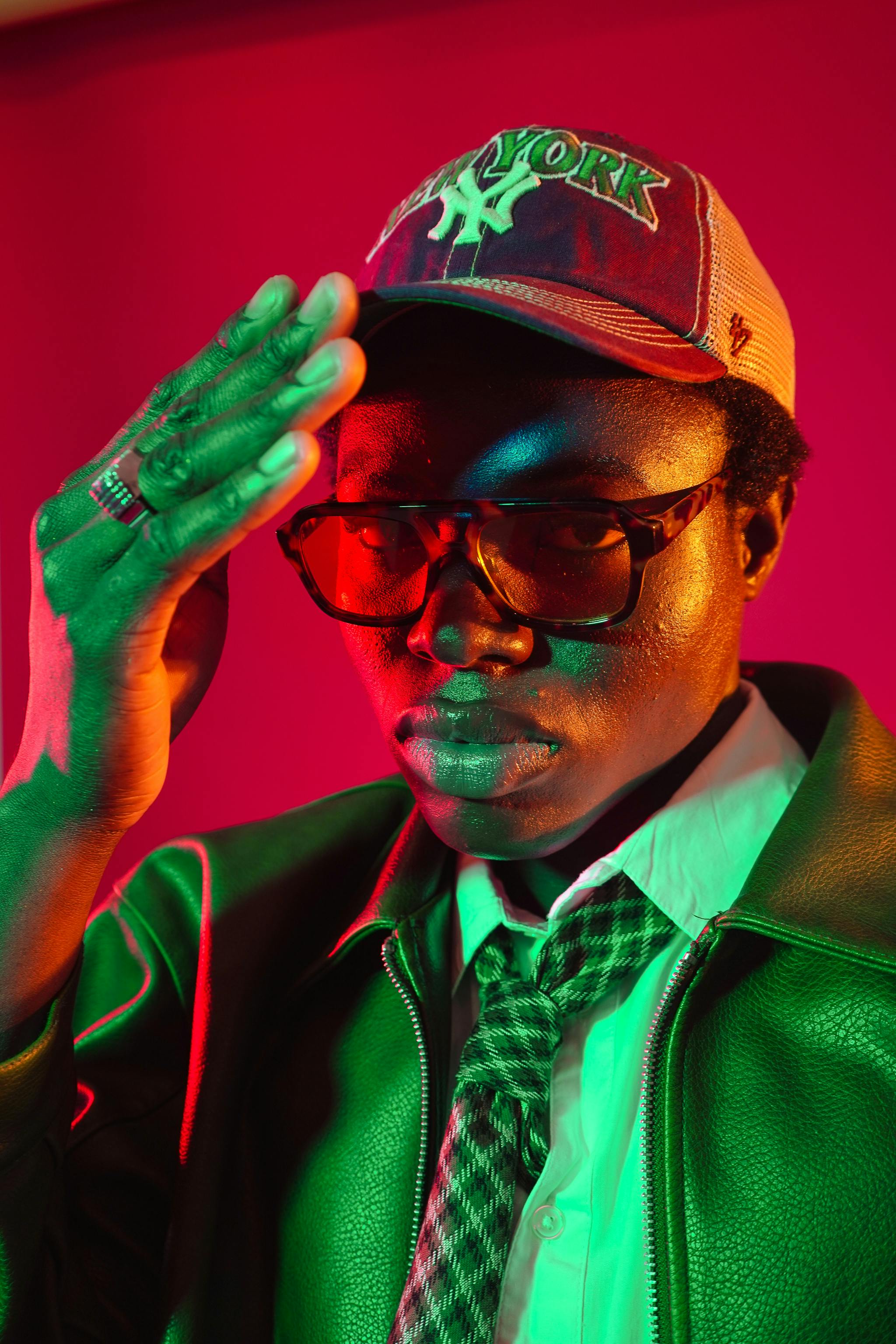 Fashion-forward portrait of a person in a cap and glasses, featuring neon lighting.