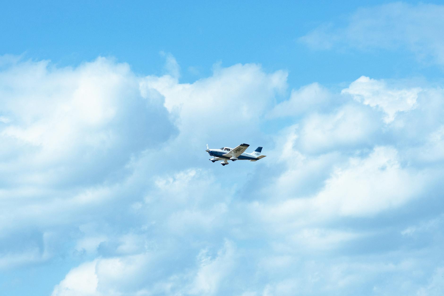 A small aircraft gliding through a vibrant blue sky with fluffy white clouds.