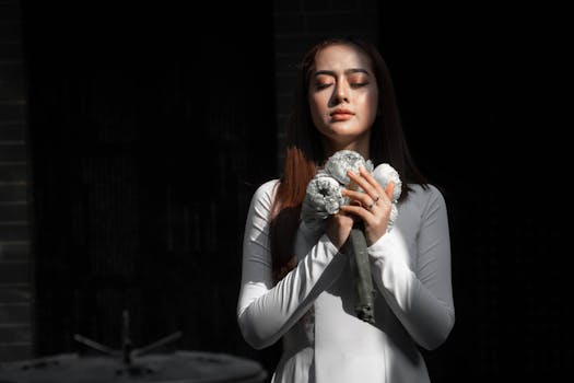 一位身穿白色连衣裙的女子，在戏剧性的灯光下闭目静立，手捧鲜花