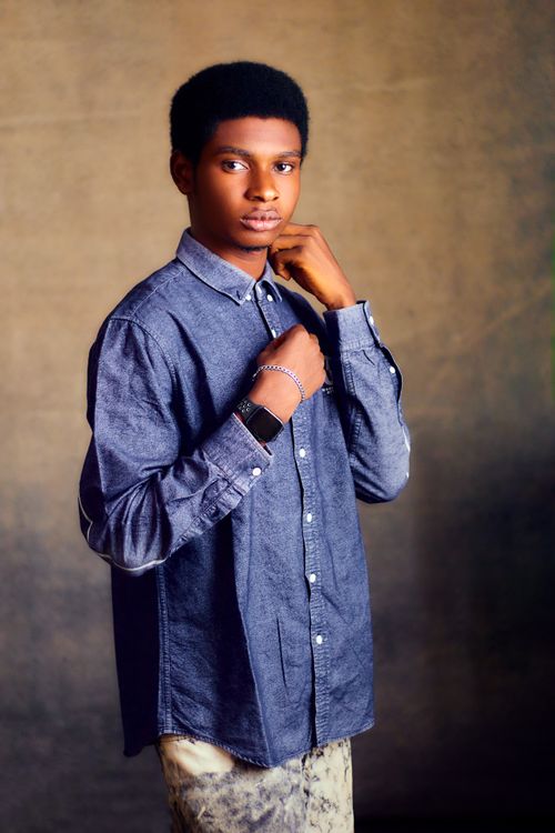 Free Young adult in denim shirt posing confidently indoors with a soft, warm background. Stock Photo