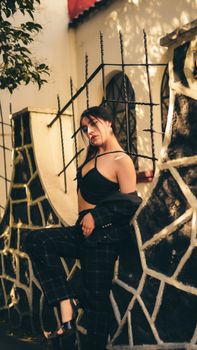 Fashionable woman poses confidently in patterned attire against outdoor architectural background.