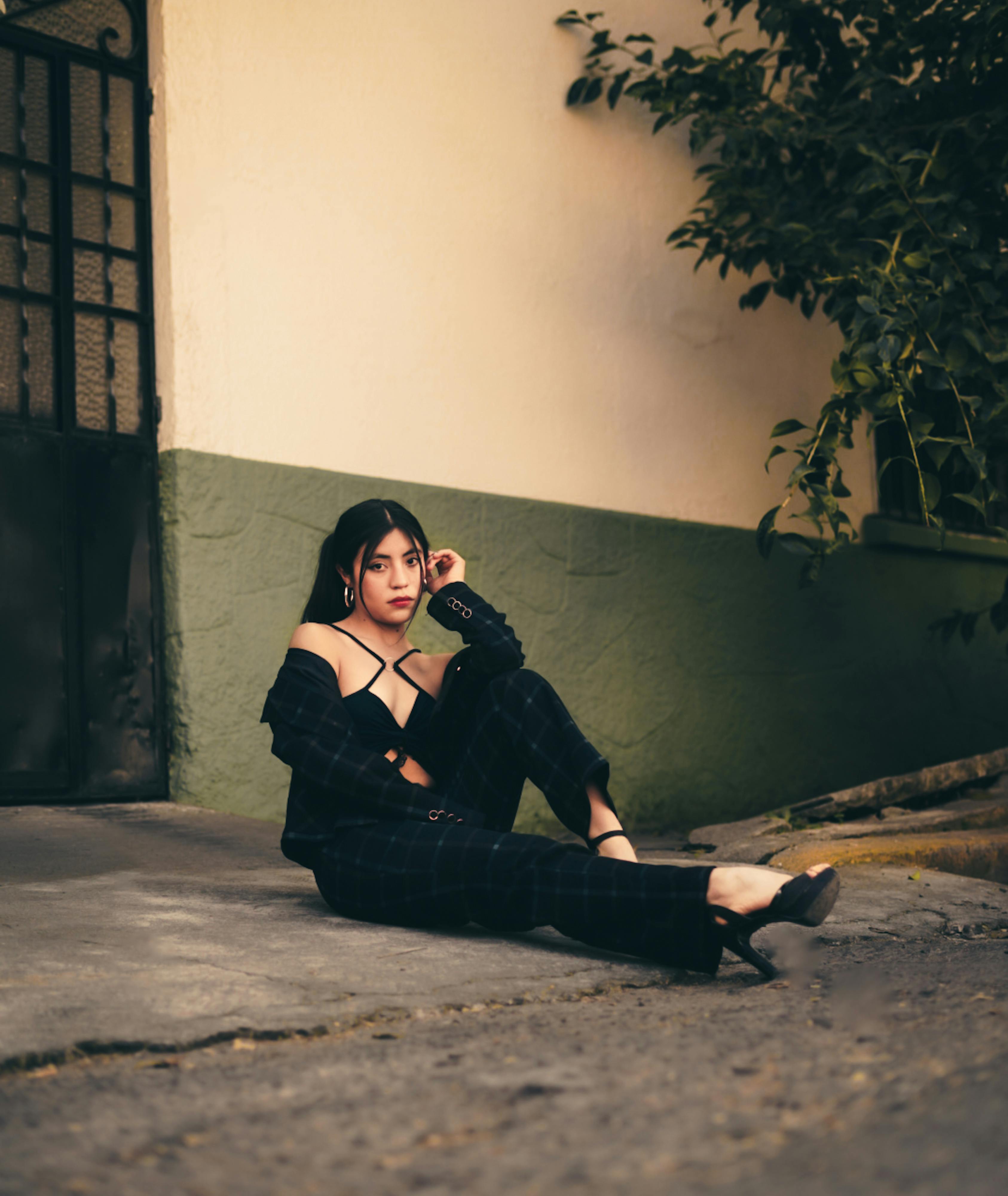 Fashionable young woman in stylish attire posing against a rustic wall, creating an urban aesthetic.