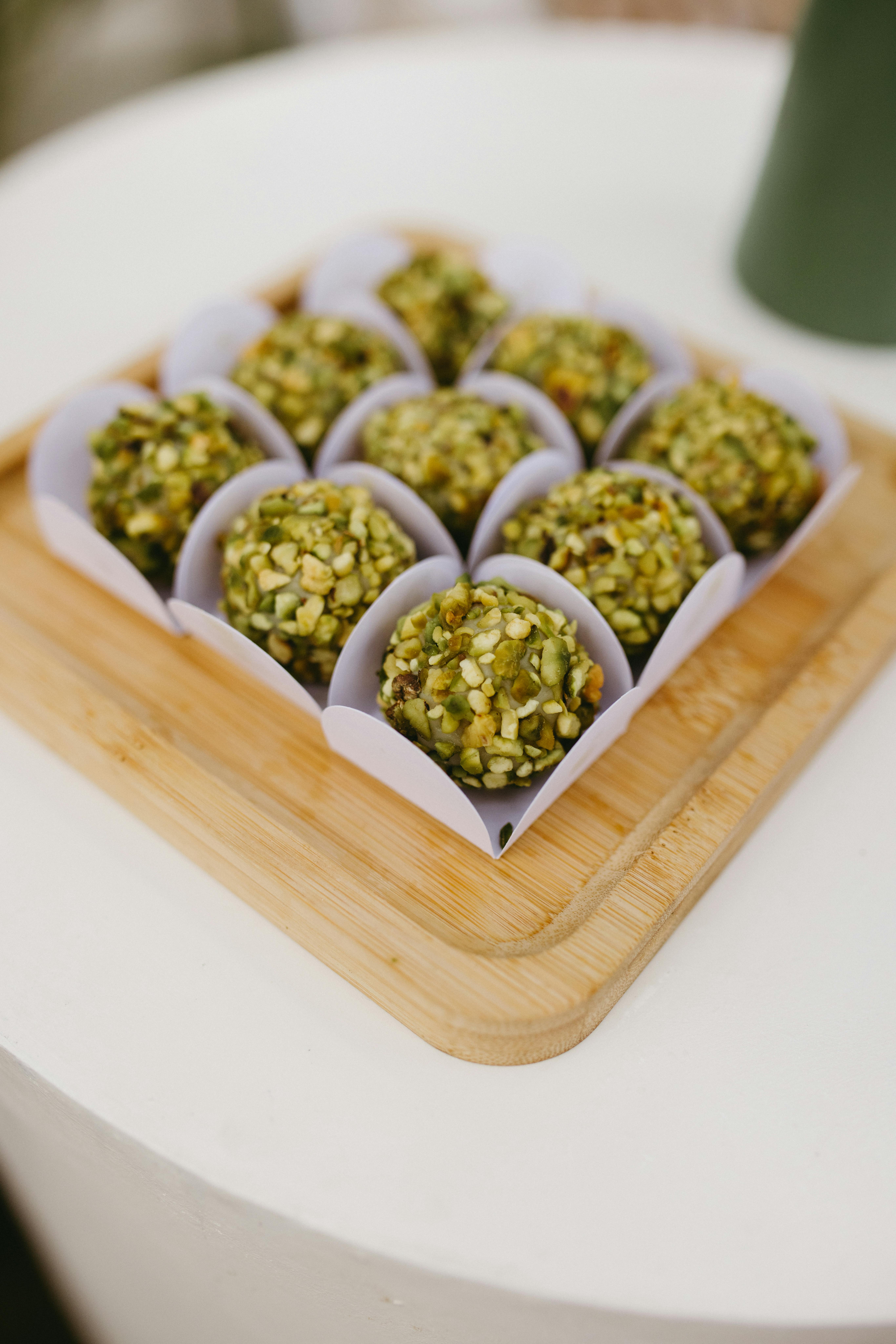 Nine pistachio-covered bonbons elegantly arranged on a wooden tray, perfect for a stylish celebration.