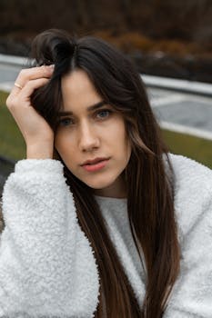 A young woman in a fluffy sweater poses thoughtfully outdoors in autumn.