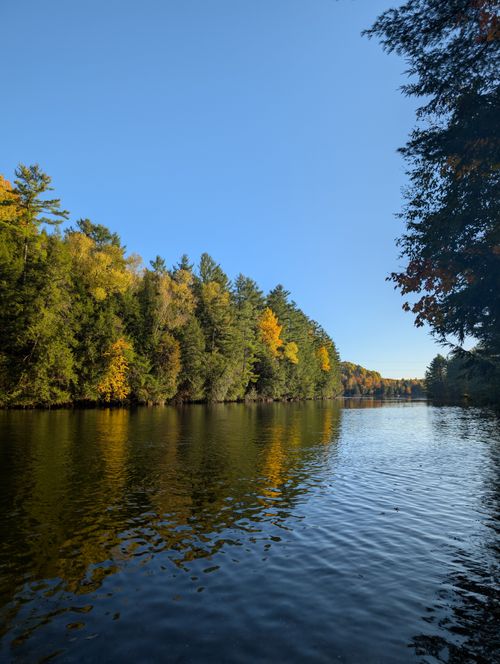 Free Tranquil river scene with autumn foliage reflecting on water. Perfect for nature and travel themes. Stock Photo