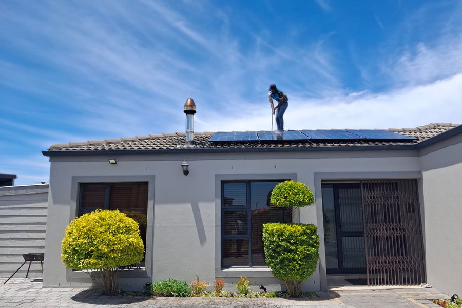 A worker installs solar panels on a house roof under a clear blue sky, showcasing renewable energy adoption.