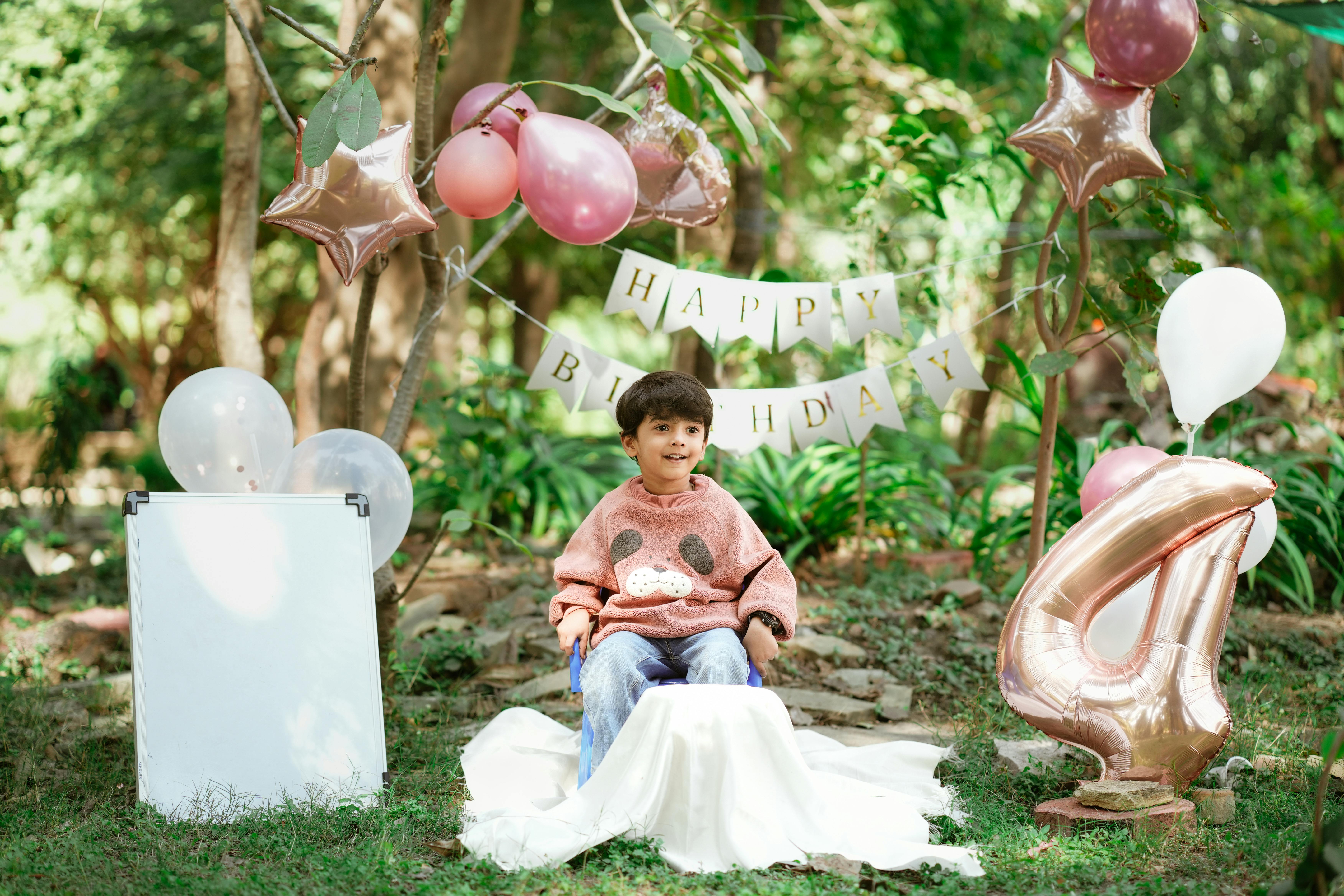 A cheerful child celebrates a birthday outdoors in Indore, India, surrounded by balloons and decorations.